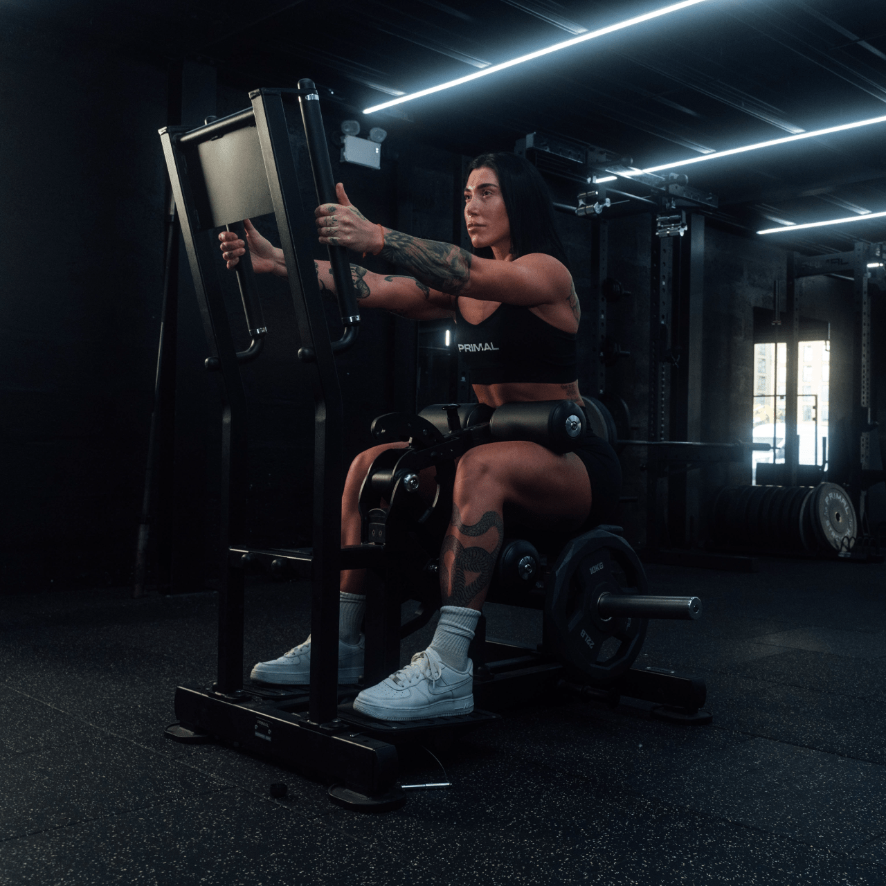 Angled view of athlete using standing hip thrust machine in seated position