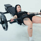 An athlete using a hip thrust pad attachment with barbell on a weight bench.