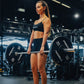 Woman lifting a barbell with 'Primal' weights in a gym setting